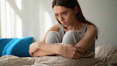 Девушка сидит на кровати обнимая колени